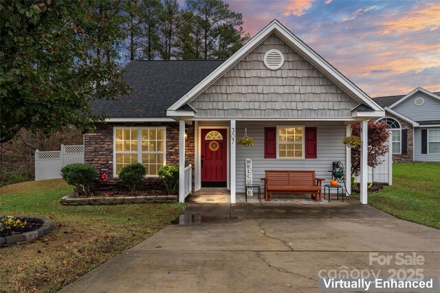 view of front of house with covered porch, a yard, stone siding, and fence