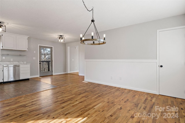 unfurnished dining area with hardwood / wood-style flooring, a textured ceiling, and a chandelier