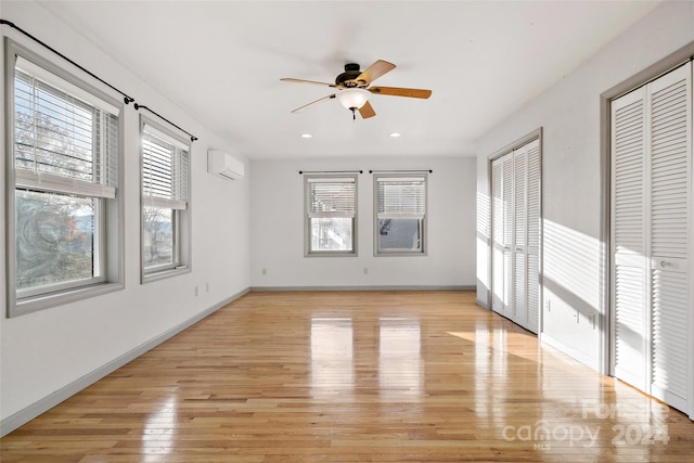 unfurnished room with a wall unit AC, a wealth of natural light, light hardwood / wood-style flooring, and ceiling fan