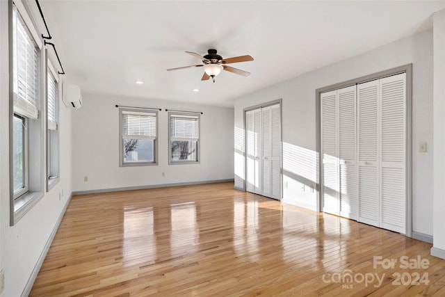 unfurnished bedroom featuring a wall mounted AC, ceiling fan, two closets, and light wood-type flooring