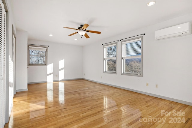 empty room with a wall mounted air conditioner, light hardwood / wood-style floors, and ceiling fan