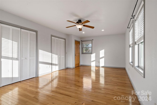 unfurnished bedroom with light wood-type flooring, two closets, and ceiling fan