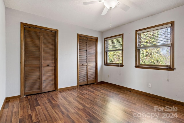 unfurnished bedroom with ceiling fan, dark hardwood / wood-style flooring, a textured ceiling, and two closets