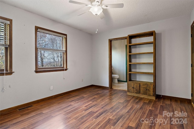 unfurnished bedroom featuring a textured ceiling, dark hardwood / wood-style floors, ceiling fan, and connected bathroom