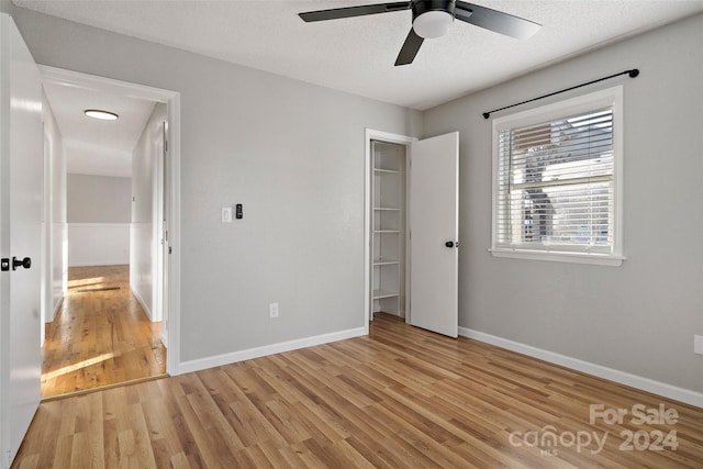 unfurnished bedroom featuring ceiling fan, a closet, a textured ceiling, and light wood-type flooring