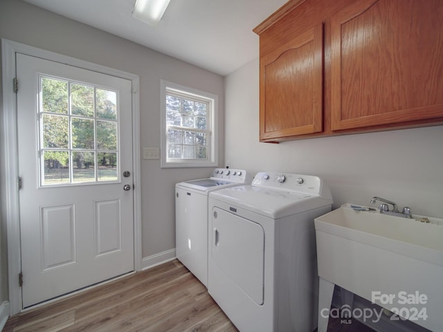 clothes washing area with cabinets, light wood-type flooring, washer and clothes dryer, and sink