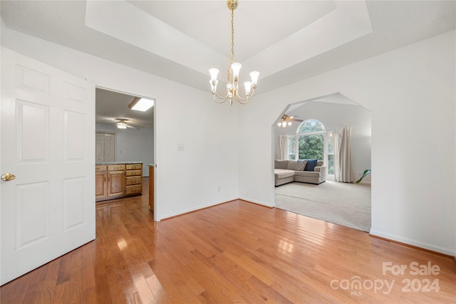 unfurnished dining area featuring hardwood / wood-style floors, ceiling fan with notable chandelier, and a raised ceiling