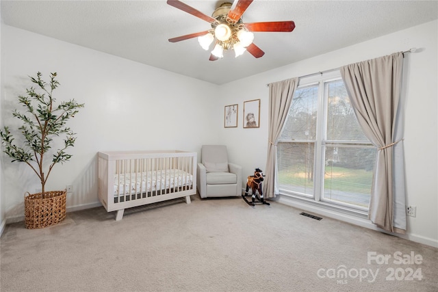 carpeted bedroom featuring a textured ceiling, ceiling fan, and a crib