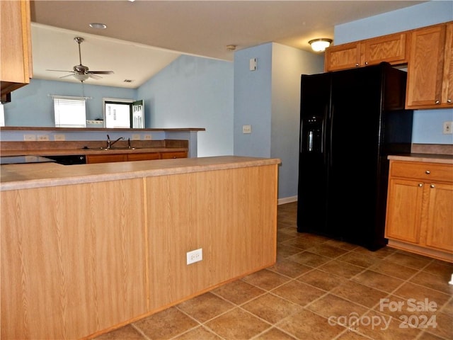 kitchen with kitchen peninsula, black fridge, ceiling fan, sink, and dark tile patterned flooring