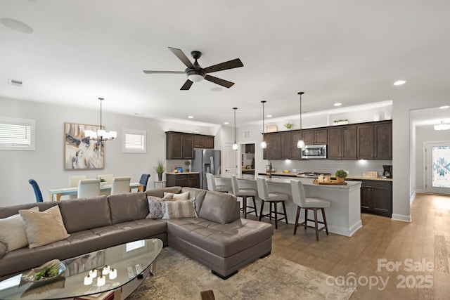 living room with ceiling fan with notable chandelier, light hardwood / wood-style flooring, and a healthy amount of sunlight