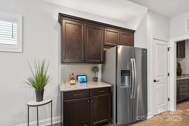 kitchen with backsplash, dark brown cabinetry, light stone countertops, and stainless steel refrigerator with ice dispenser