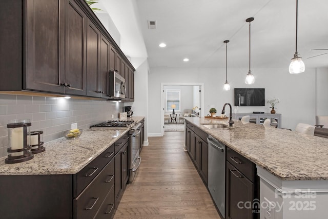 kitchen with light stone counters, dark brown cabinets, stainless steel appliances, a kitchen island with sink, and sink