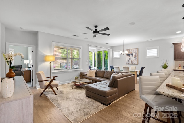 living room featuring ceiling fan with notable chandelier, light hardwood / wood-style flooring, and plenty of natural light