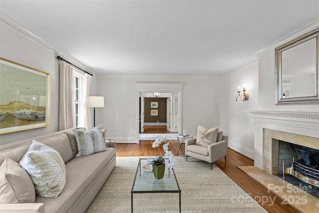 living area with crown molding, wood finished floors, baseboards, and a fireplace with raised hearth