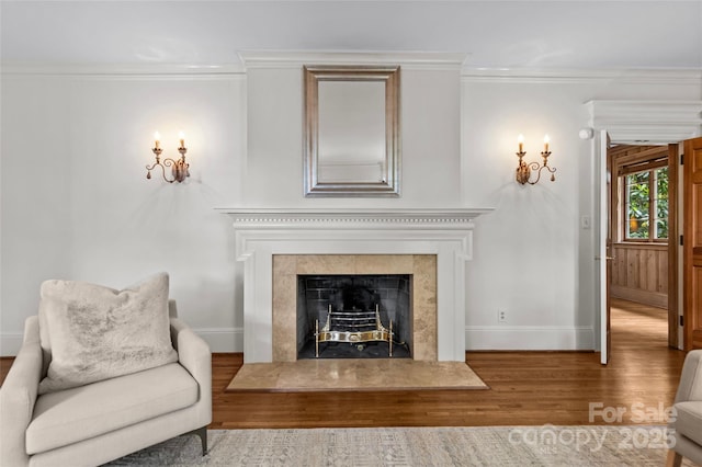 living area featuring wood finished floors, baseboards, crown molding, and a fireplace with raised hearth