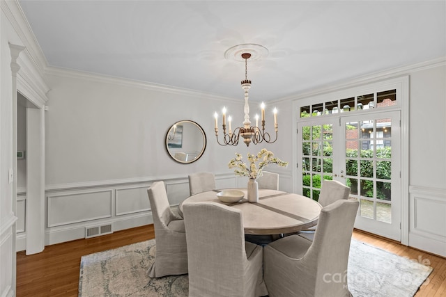 dining area featuring wood finished floors, a chandelier, crown molding, a wainscoted wall, and a decorative wall