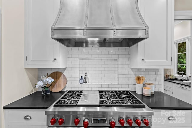 kitchen featuring under cabinet range hood, a sink, stainless steel range, dark countertops, and white cabinets