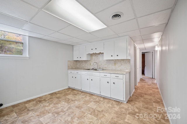 kitchen with tasteful backsplash, sink, white cabinets, and a drop ceiling