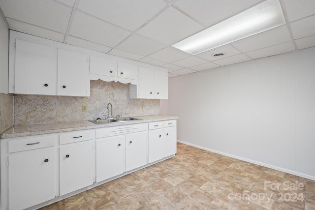 kitchen with a drop ceiling, white cabinetry, sink, and tasteful backsplash