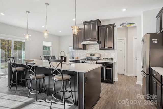 kitchen featuring stainless steel appliances, pendant lighting, a breakfast bar area, a center island with sink, and light wood-type flooring