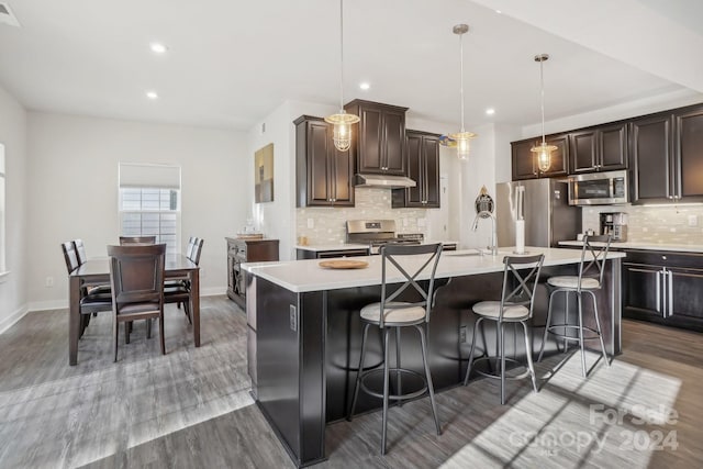 kitchen featuring hardwood / wood-style floors, a center island with sink, hanging light fixtures, a breakfast bar area, and stainless steel appliances