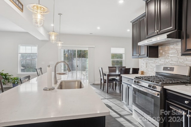 kitchen with tasteful backsplash, gas stove, sink, decorative light fixtures, and an island with sink