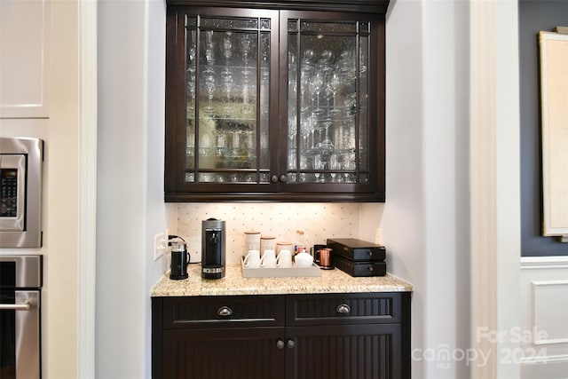 bar featuring light stone countertops, dark brown cabinetry, stainless steel appliances, and tasteful backsplash