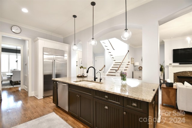 kitchen with dark brown cabinetry, stainless steel appliances, sink, decorative light fixtures, and light hardwood / wood-style floors