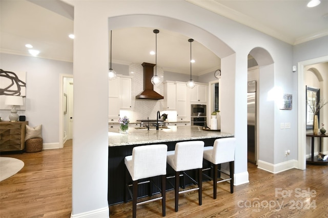 kitchen with white cabinets, pendant lighting, wall chimney range hood, and hardwood / wood-style floors