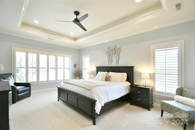 carpeted bedroom with a raised ceiling, multiple windows, and ceiling fan