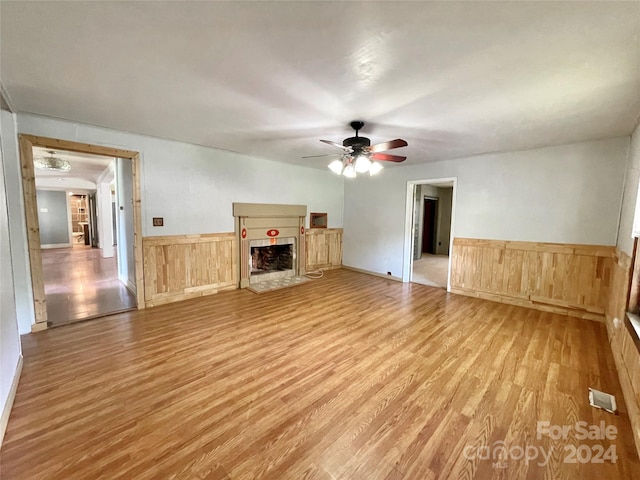 unfurnished living room with ceiling fan, wooden walls, and hardwood / wood-style flooring