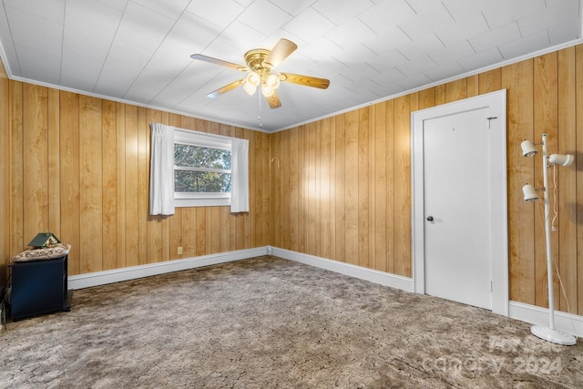 carpeted empty room with ceiling fan, wood walls, and crown molding