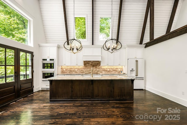 kitchen featuring a kitchen island with sink, decorative backsplash, white appliances, high vaulted ceiling, and a sink