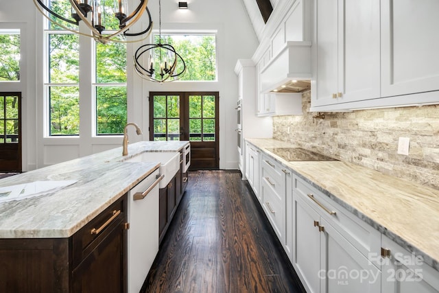 kitchen with premium range hood, a sink, white cabinetry, backsplash, and a chandelier