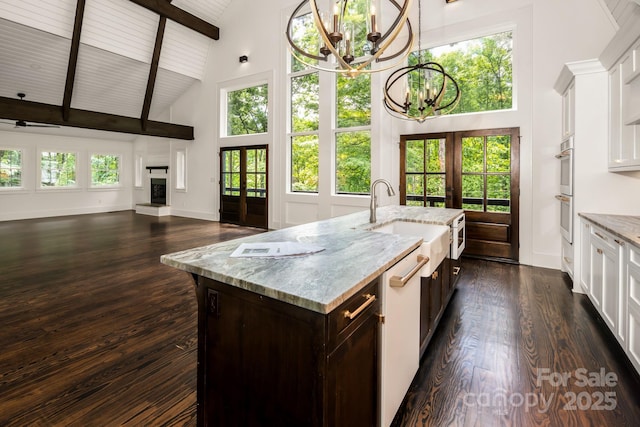 kitchen with high vaulted ceiling, a fireplace with raised hearth, open floor plan, french doors, and white cabinets