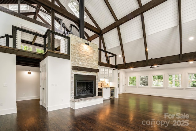 unfurnished living room with beverage cooler, baseboards, a stone fireplace, dark wood-type flooring, and beamed ceiling