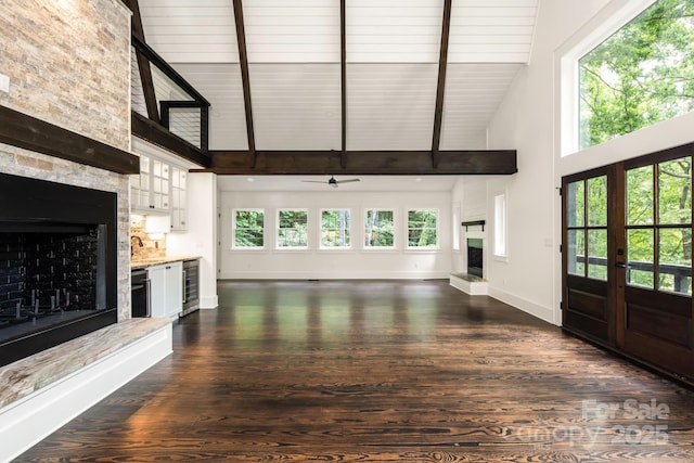 unfurnished living room with beverage cooler, baseboards, high vaulted ceiling, dark wood finished floors, and a large fireplace