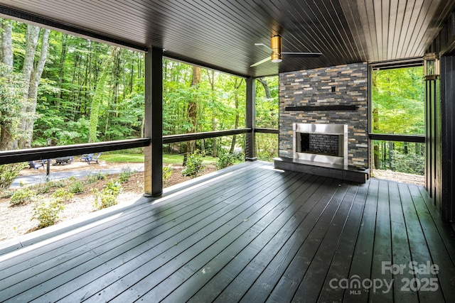 unfurnished sunroom with a stone fireplace and ceiling fan