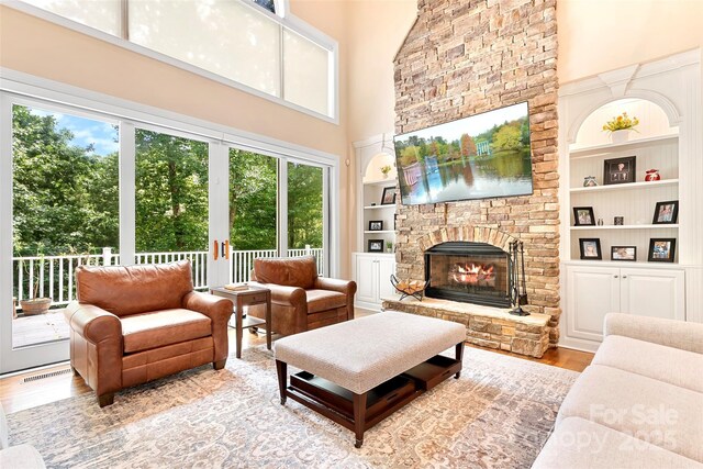 living room with built in shelves, a towering ceiling, a fireplace, and light hardwood / wood-style flooring