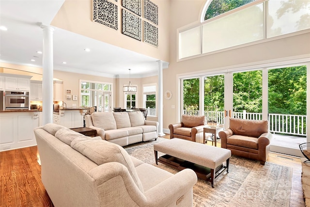 living room featuring ornamental molding, a high ceiling, light hardwood / wood-style flooring, and ornate columns