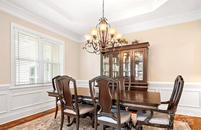 dining room with a raised ceiling, ornamental molding, hardwood / wood-style floors, and a notable chandelier