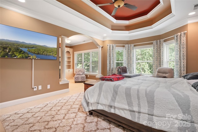 bedroom featuring ornamental molding, a tray ceiling, decorative columns, and multiple windows