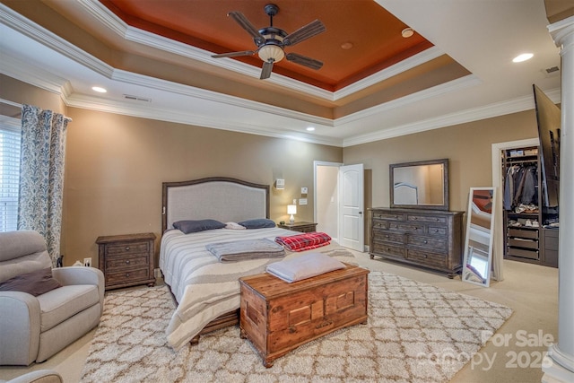 bedroom with crown molding, a walk in closet, a raised ceiling, a closet, and light colored carpet