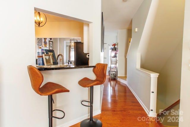 bar featuring a chandelier, stainless steel fridge, hardwood / wood-style floors, and hanging light fixtures