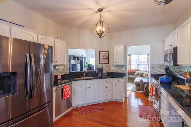 kitchen with pendant lighting, hardwood / wood-style floors, white cabinets, sink, and stainless steel appliances