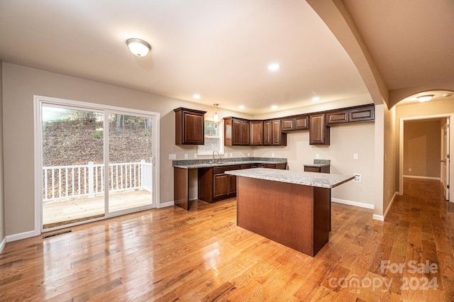 kitchen featuring sink, light stone countertops, light hardwood / wood-style floors, decorative light fixtures, and a kitchen island