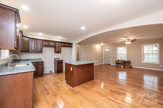 kitchen featuring sink, ceiling fan, light wood-type flooring, light stone countertops, and a kitchen island