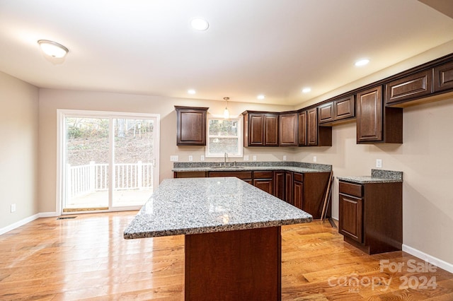 kitchen featuring hanging light fixtures, light wood-type flooring, dark brown cabinets, a kitchen island, and light stone counters