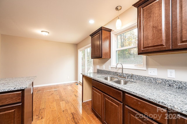 kitchen with light stone countertops, light hardwood / wood-style flooring, hanging light fixtures, and sink