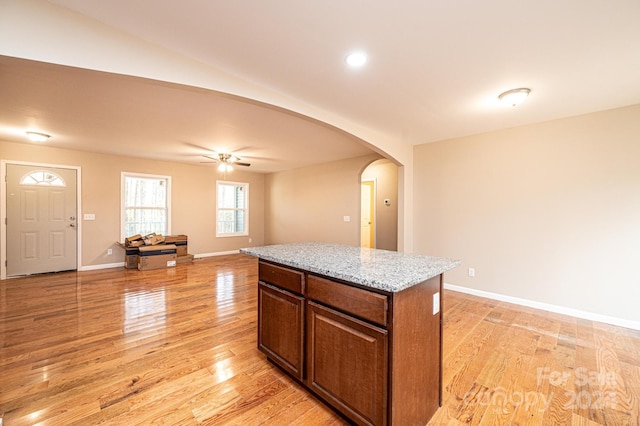 kitchen with light stone countertops, light wood-type flooring, vaulted ceiling, ceiling fan, and a kitchen island